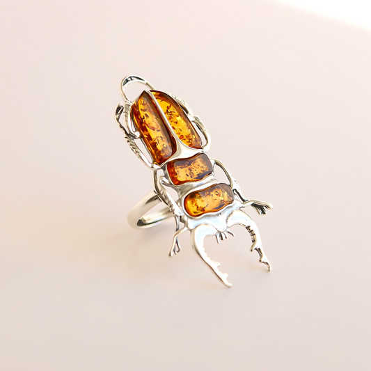 Silver scarab ring with amber stones on a light pink background