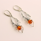 Pair of silver spider earrings with amber-colored gemstones on a light pink background