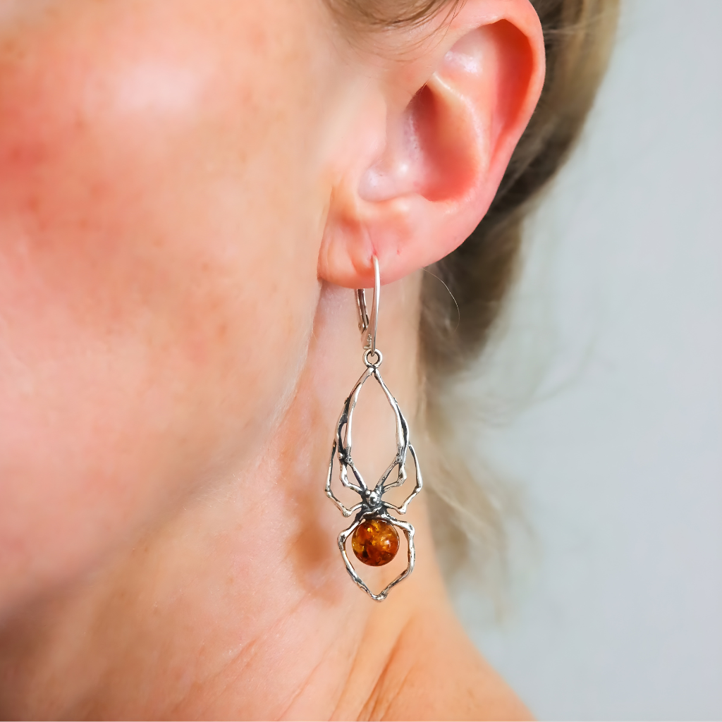 Silver spider earrings with a brown gemstone worn by a person.