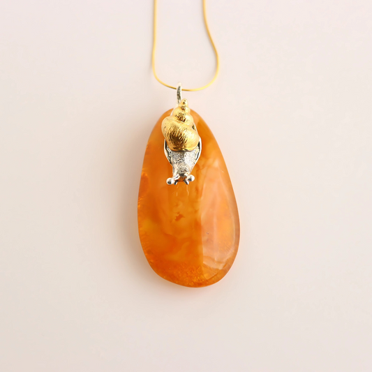 Orange teardrop-shaped pendant statement necklace with gold and silver accents on a beige background