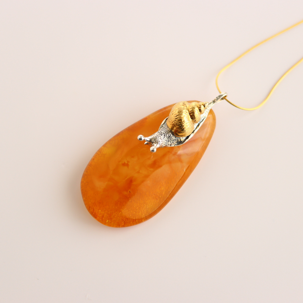 Orange teardrop-shaped pendant statement necklace with gold and silver accents on a beige background