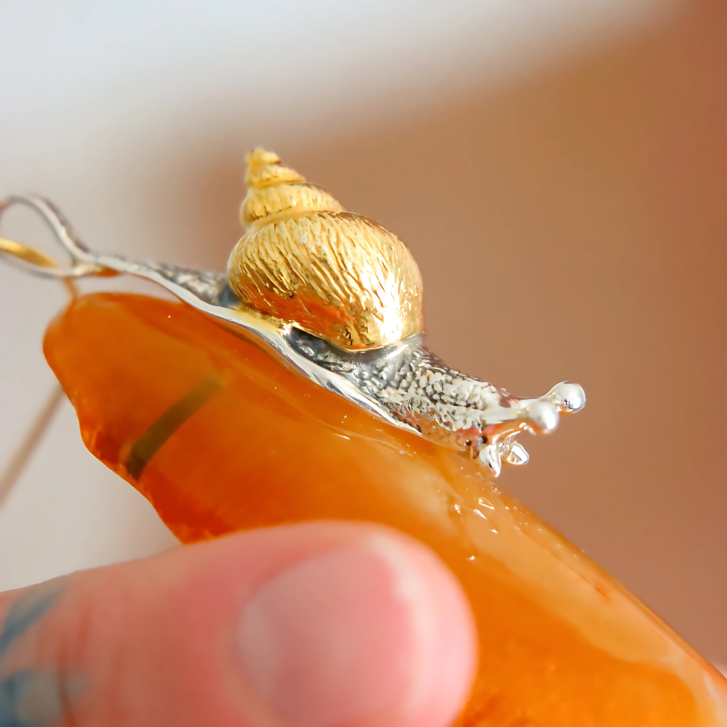 statement necklace with a gold snail shell and orange stone held by a hand.