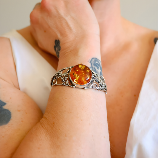 Close-up of a wrist wearing a stelring silver bracelet with an amber stone, against a neutral background.