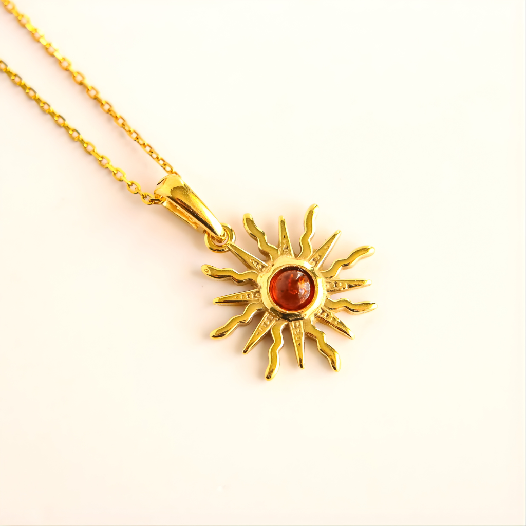 Gold amber sun necklace with a red gemstone on a light pink background