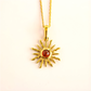 Gold  amber sun necklace with a red gemstone on a light pink background