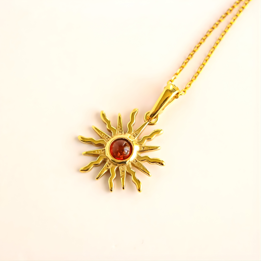Gold amber sun necklace with a red gemstone on a light pink background