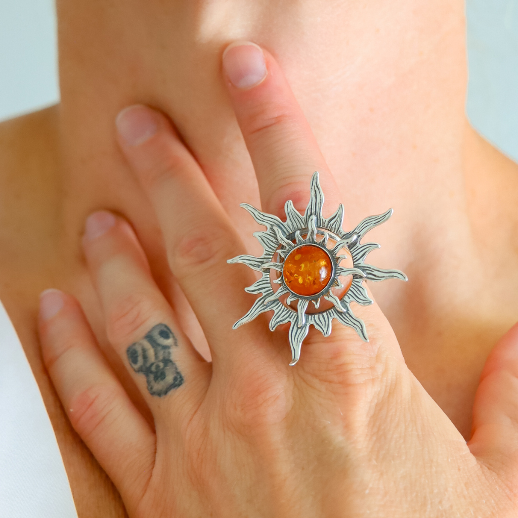 Silver sun ring with a red stone on a person's finger against a light background