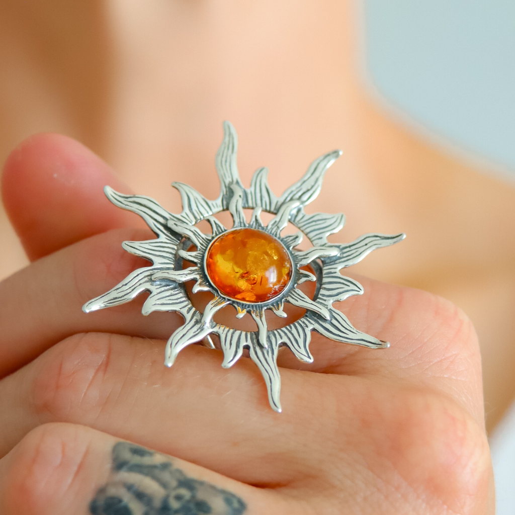 Silver sun ring with a central amber stone held in a hand.