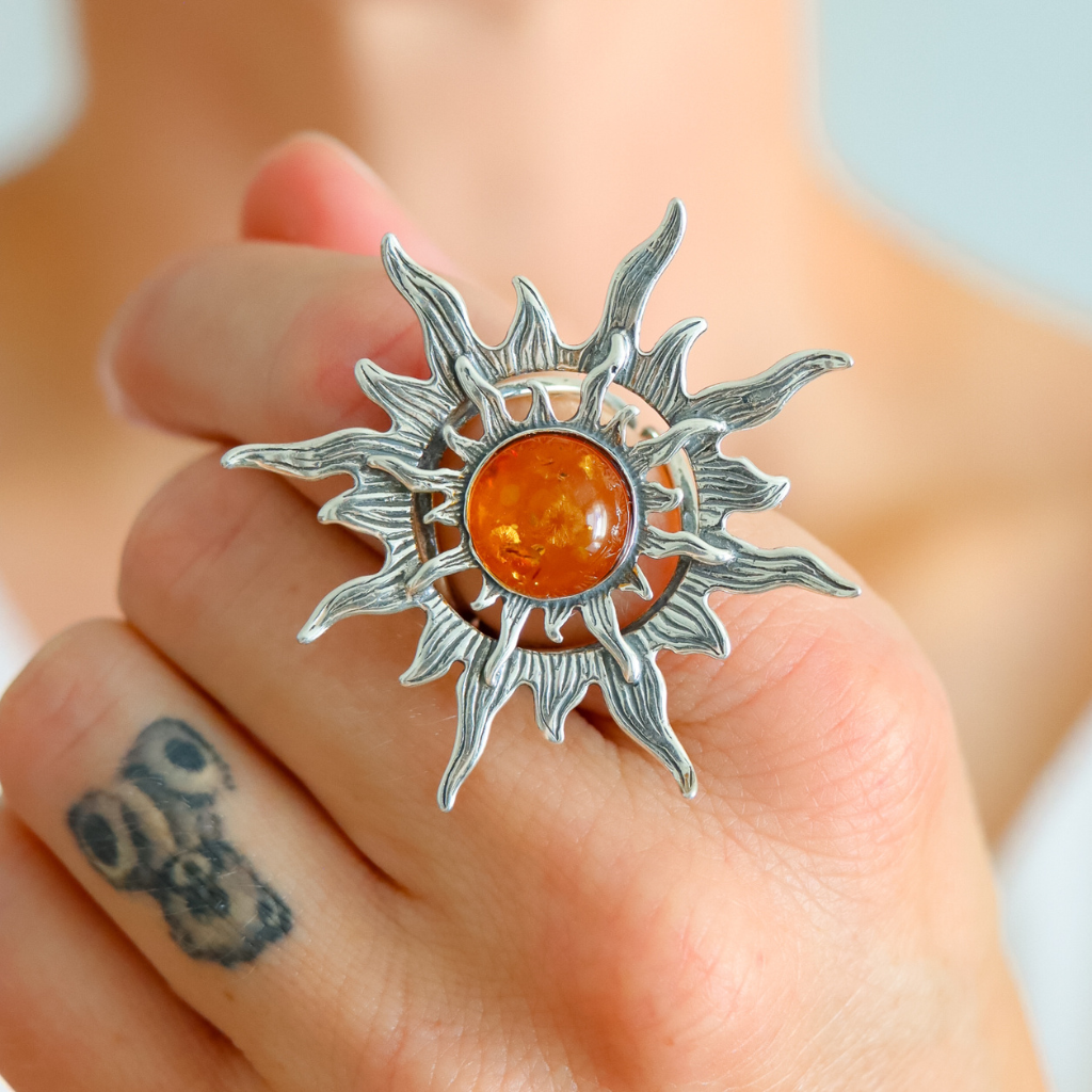 Silver sun ring with a amber stone held on a hand