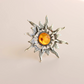Silver sun ring with a orange gemstone on a beige background
