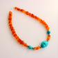 beaded Necklace with orange beads and a turquoise stone on a light background