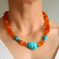 Beaded Necklace with orange beads and a large turquoise stone worn by a person.