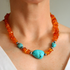 Beaded Necklace with orange beads and a large turquoise stone worn by a person.