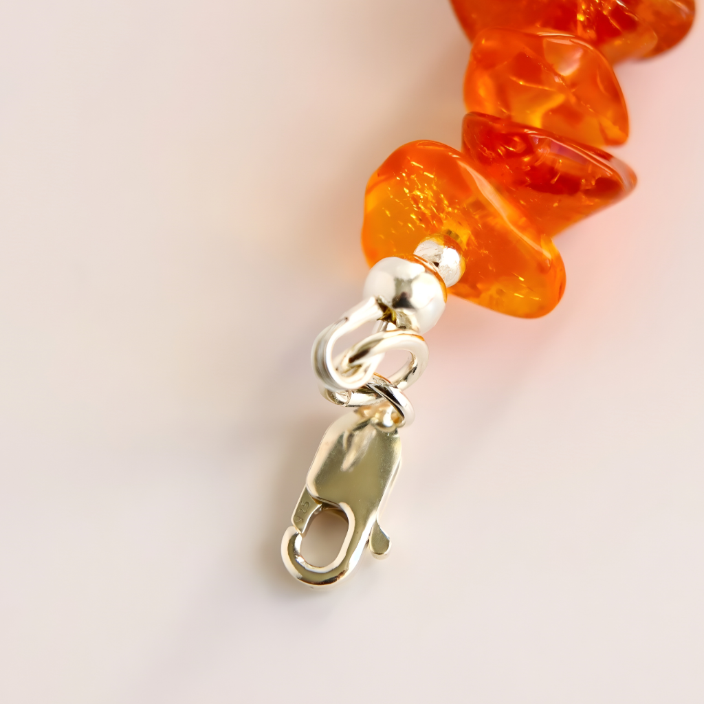 Close-up of orange beaded necklace with a silver clasp on a light background