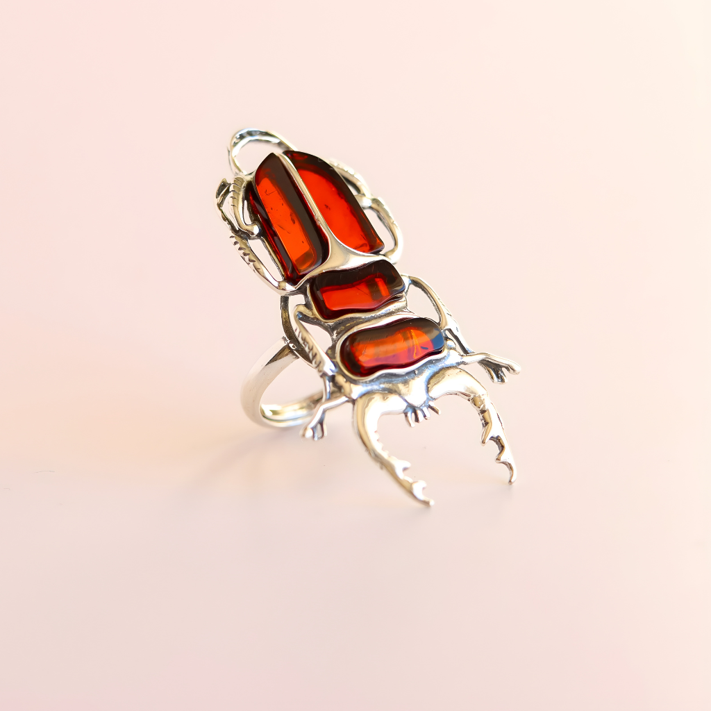 Silver scarab beetle amber ring with red gemstones on a light pink background