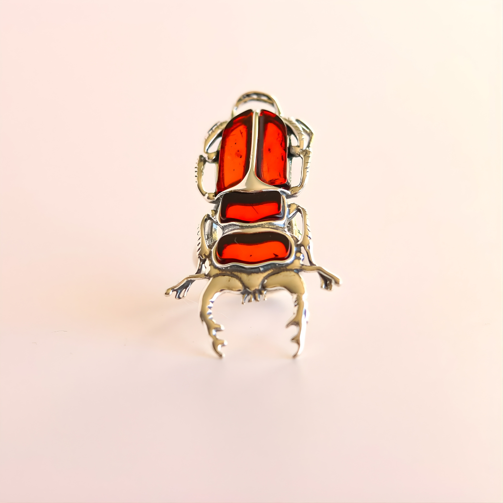 scarab-shaped amber necklace with red and silver details on a light pink background