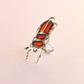 Silver and red scarab beetle-shaped amber ring on a pink background