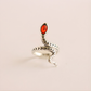 Silver snake-shaped ring with a red stone on a beige background