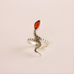Silver snake-shaped ring with a red stone on a beige background