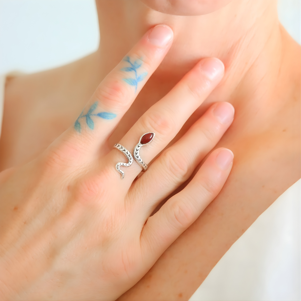 Close-up of a hand wearing a silver snake ring with a red stone on a light background