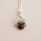 Silver spider charm necklace with a red gemstone on a beige background