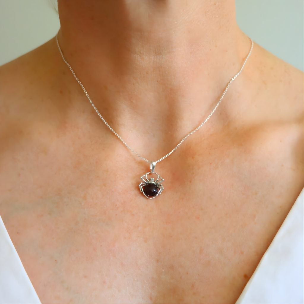 Silver spider charm necklace with a heart-shaped pendant worn by a person