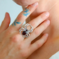 Silver spider ring with a red gemstone on a person's finger.