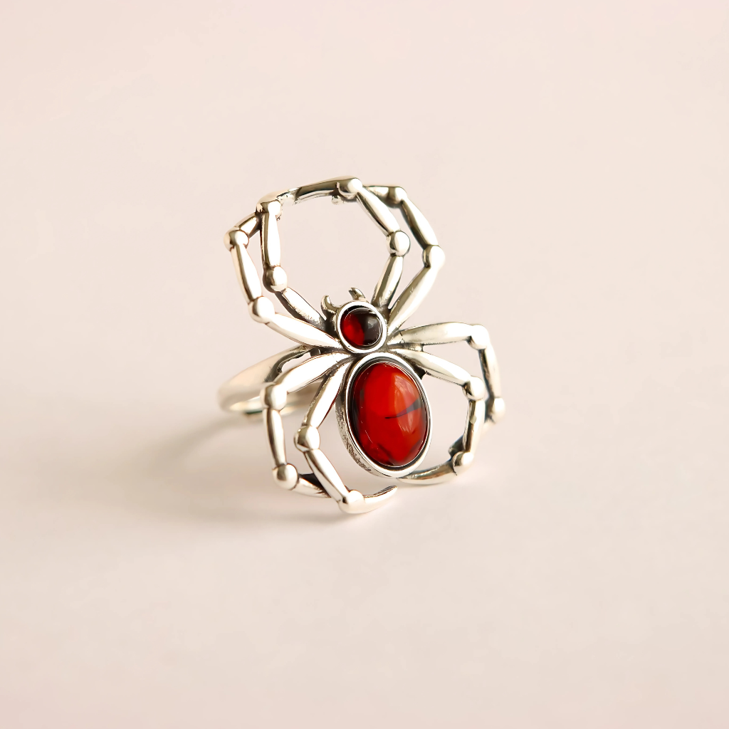 Silver spider ring with red gemstones on a beige background