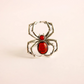 Silver spider ring with red center on a beige background