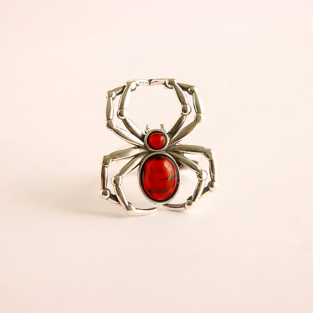 Silver spider ring with red center on a beige background