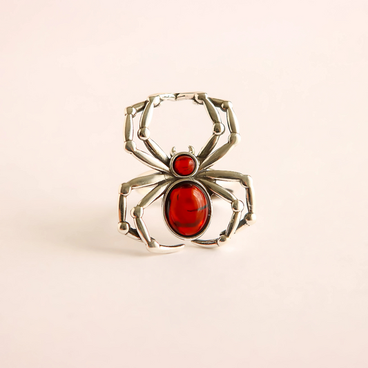 Silver spider ring with red center on a beige background