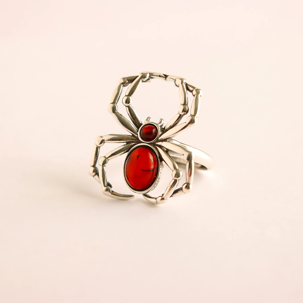 Silver spider ring with red stone on a beige background