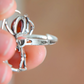 Silver spider ring with a red stone held between fingers against a blurred background