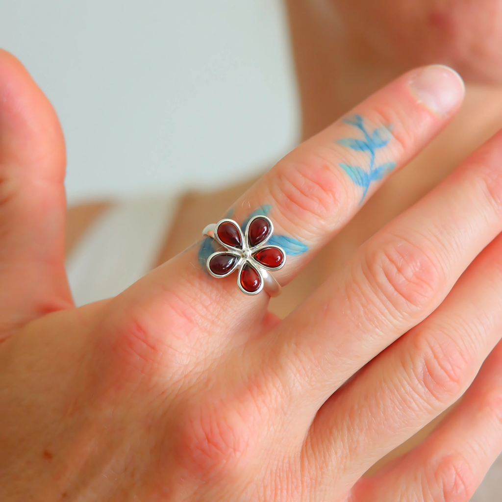 Hand wearing a silver ring with a red gemstone on a light background