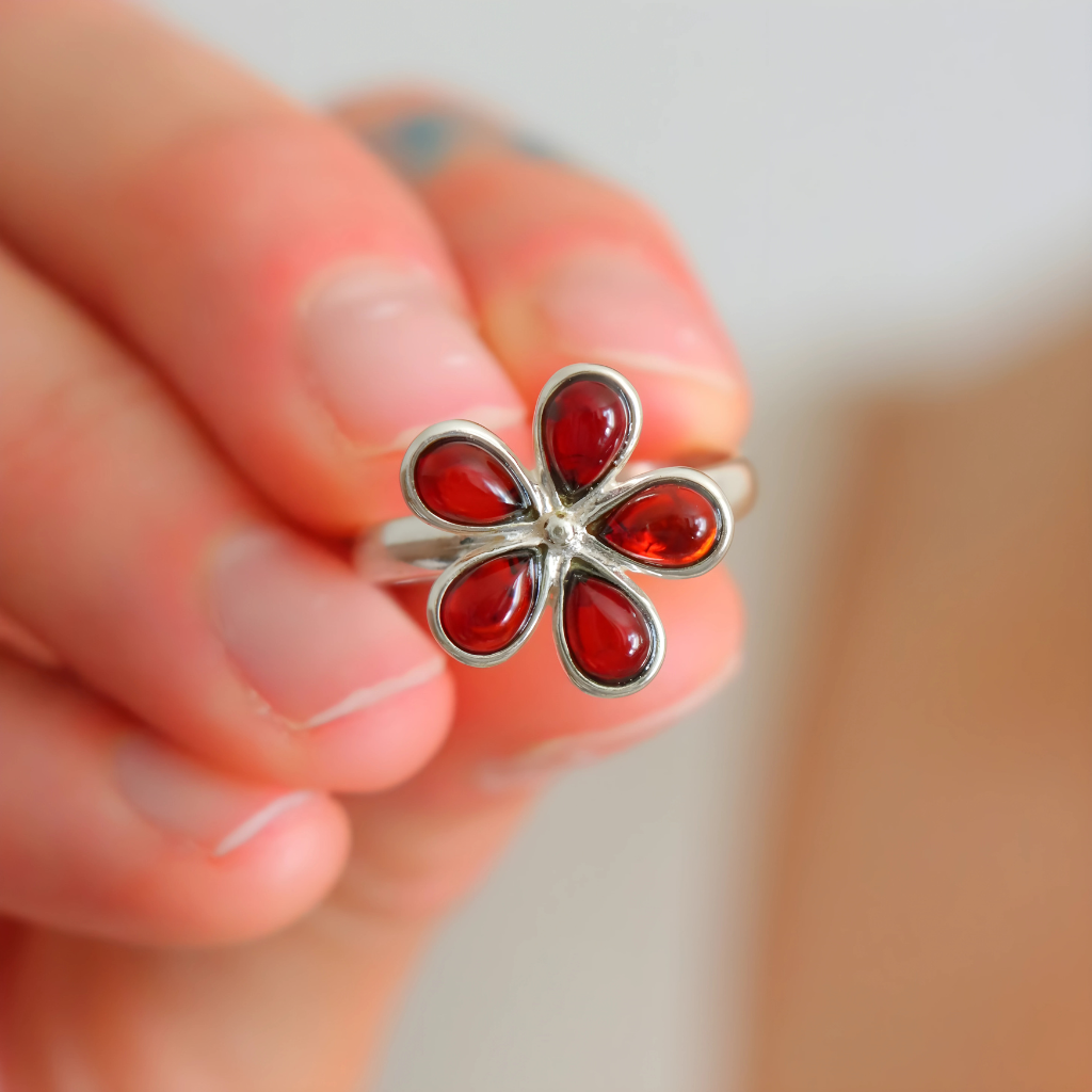 Silver ring with red gemstones held in a hand against a blurred background