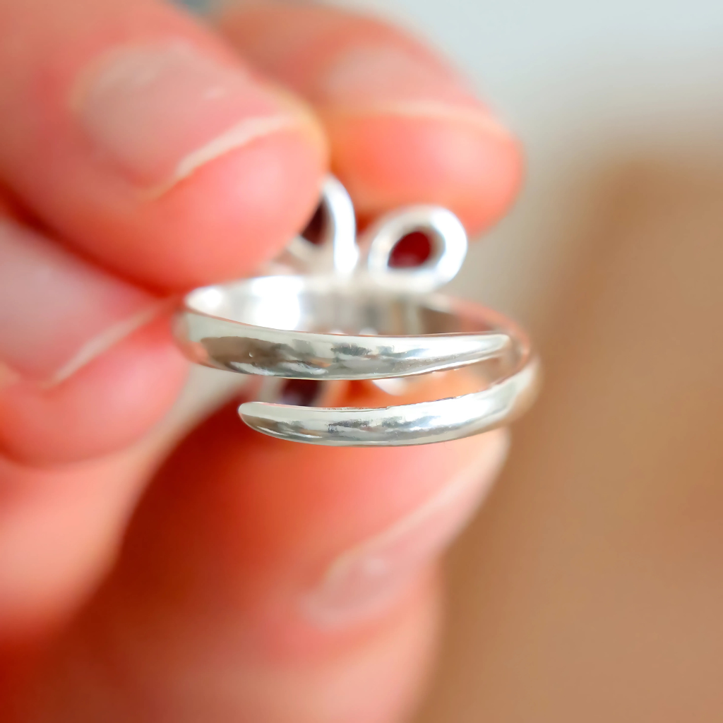 Silver spiral ring held between fingers with a blurred background