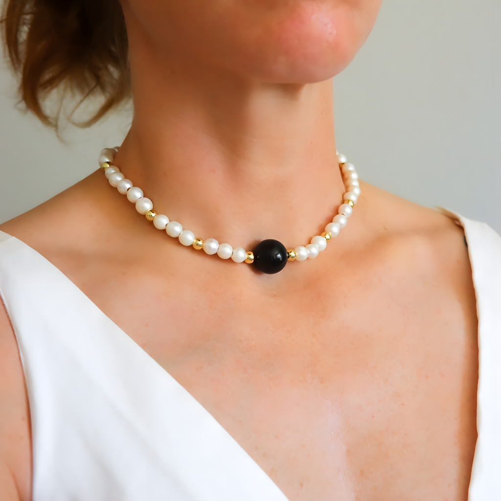Pearl necklace with a black bead worn by a person against a neutral background