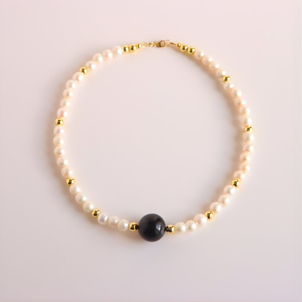 Pearl necklace with a black bead on a light pink background