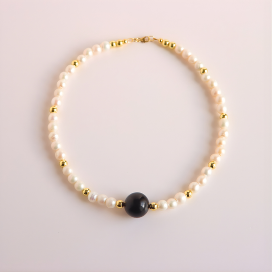 Pearl necklace with a black bead on a light pink background