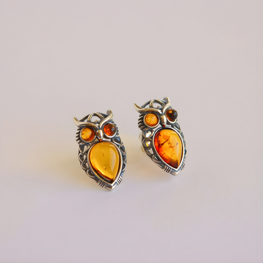 Pair of amber owl earrings with amber stones on a light gray background