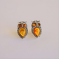 Pair of amber owl earrings with amber-colored stones on a light gray background