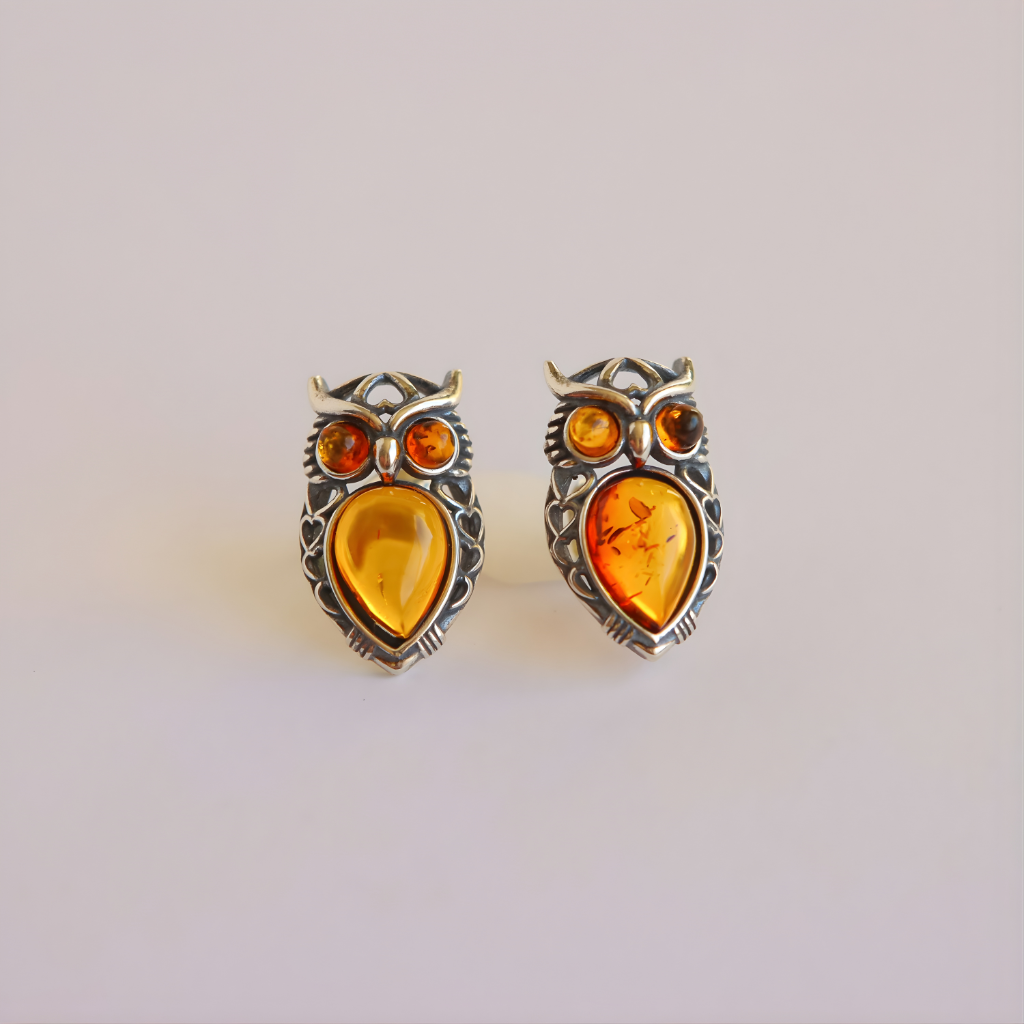 Pair of amber owl earrings with amber-colored stones on a light gray background