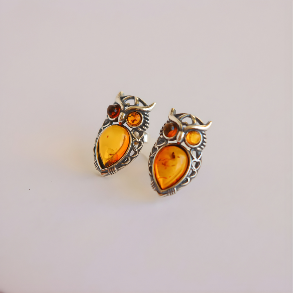 Pair of amber owl earrings with amber-colored stones on a light gray background