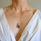 Necklace with a amber pendant featuring a red stone and silver design on a white top.