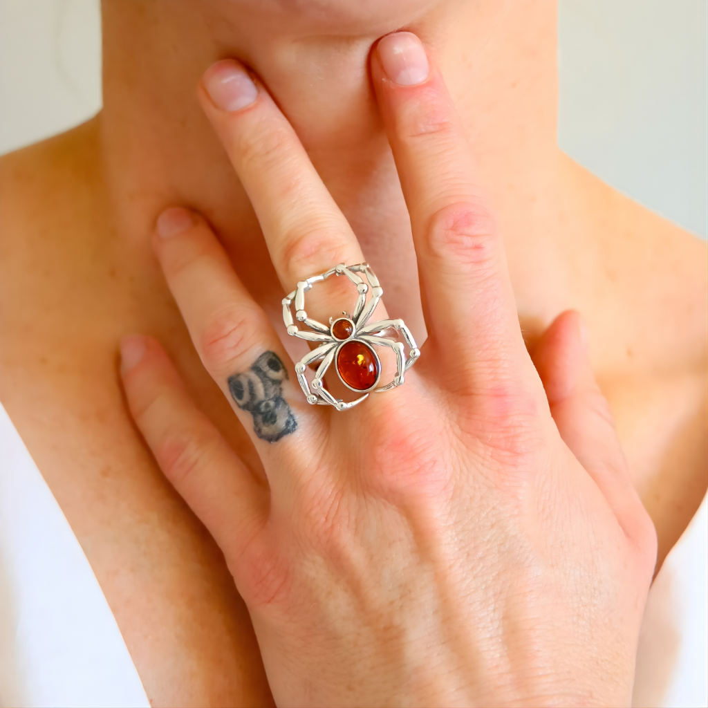 Silver ring amber with a red gemstone worn on a finger, with a tattoo visible on the other hand.
