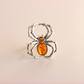 Silver spider-shaped amber ring with orange gemstones on a beige background