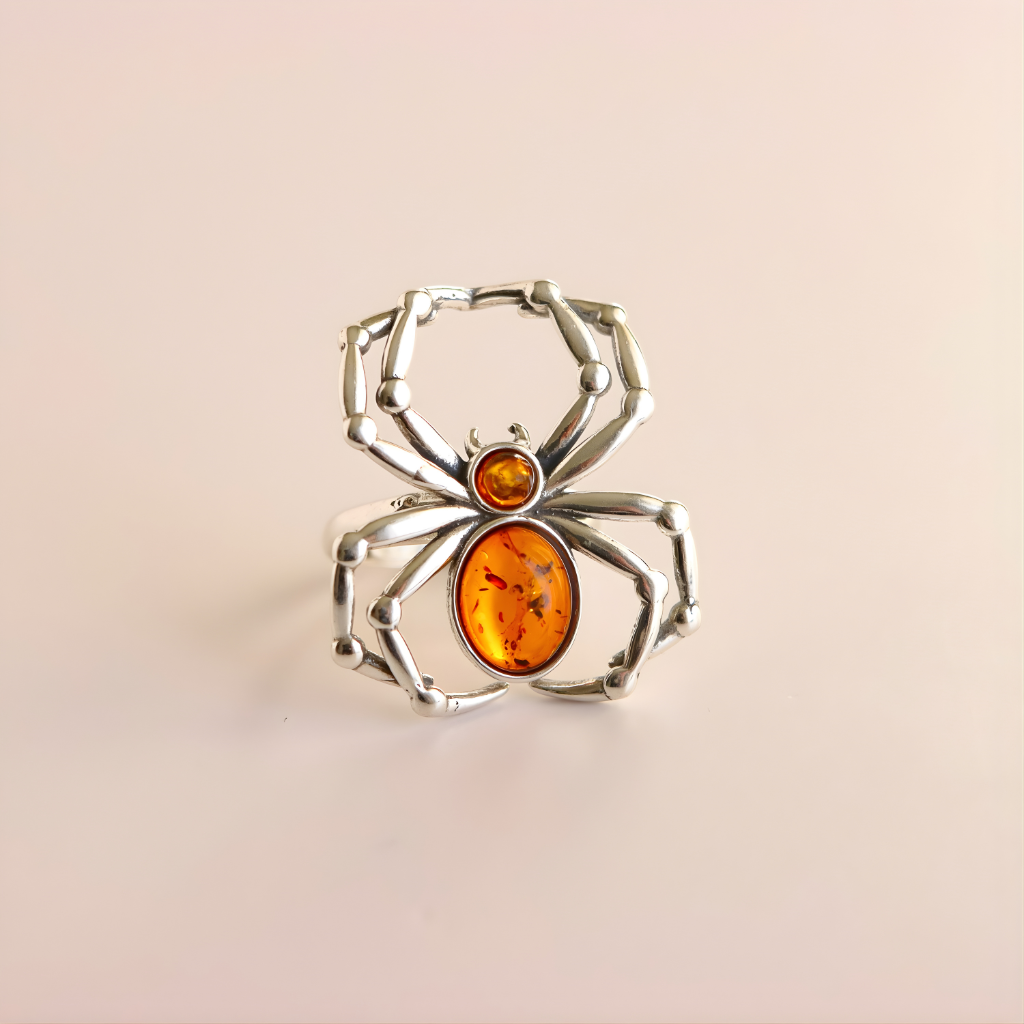 Silver spider-shaped amber ring with orange gemstones on a beige background