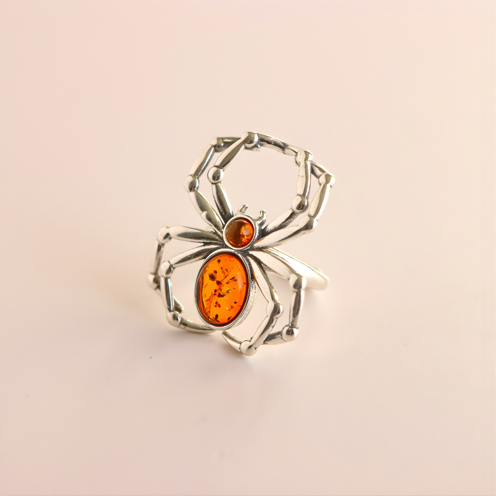 Silver spider-shaped amber ring with amber stones on a beige background