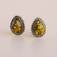 Pair of amber teardrop clip on earrings with silver settings on a light background