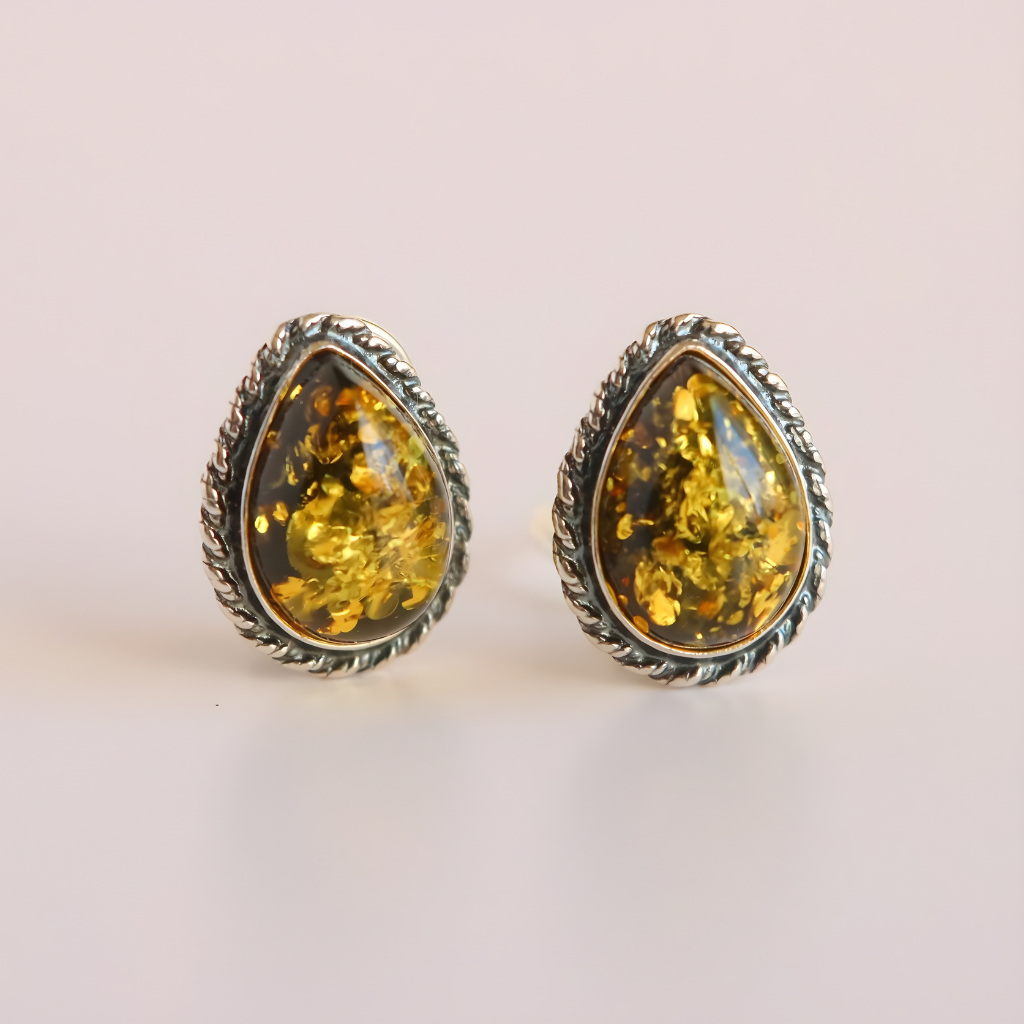 Pair of amber teardrop clip on earrings with silver frames on a light pink background